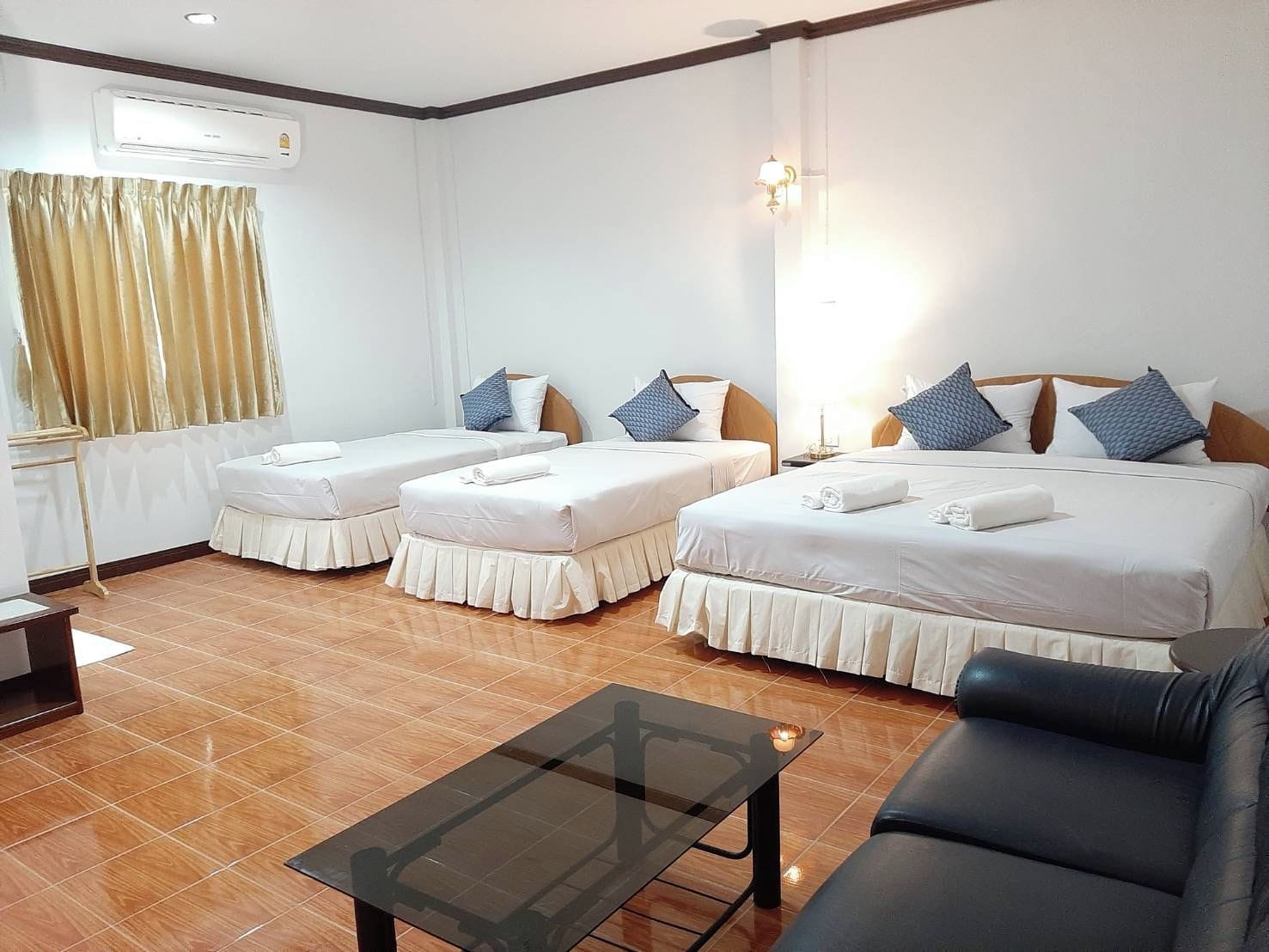 A hotel room with two single beds, a sofa, a glass-top table, and a window with curtains.