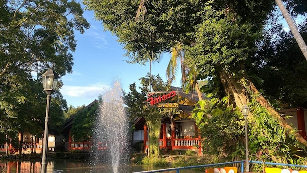 A riverside restaurant with outdoor seating, a fountain, and a sign with Thai script. - Chakdaw Mountain View Resort (Nakhon Nayok)