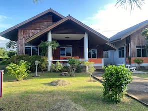 A two-story building with a wooden facade, a balcony, and a well-maintained garden with various plants.