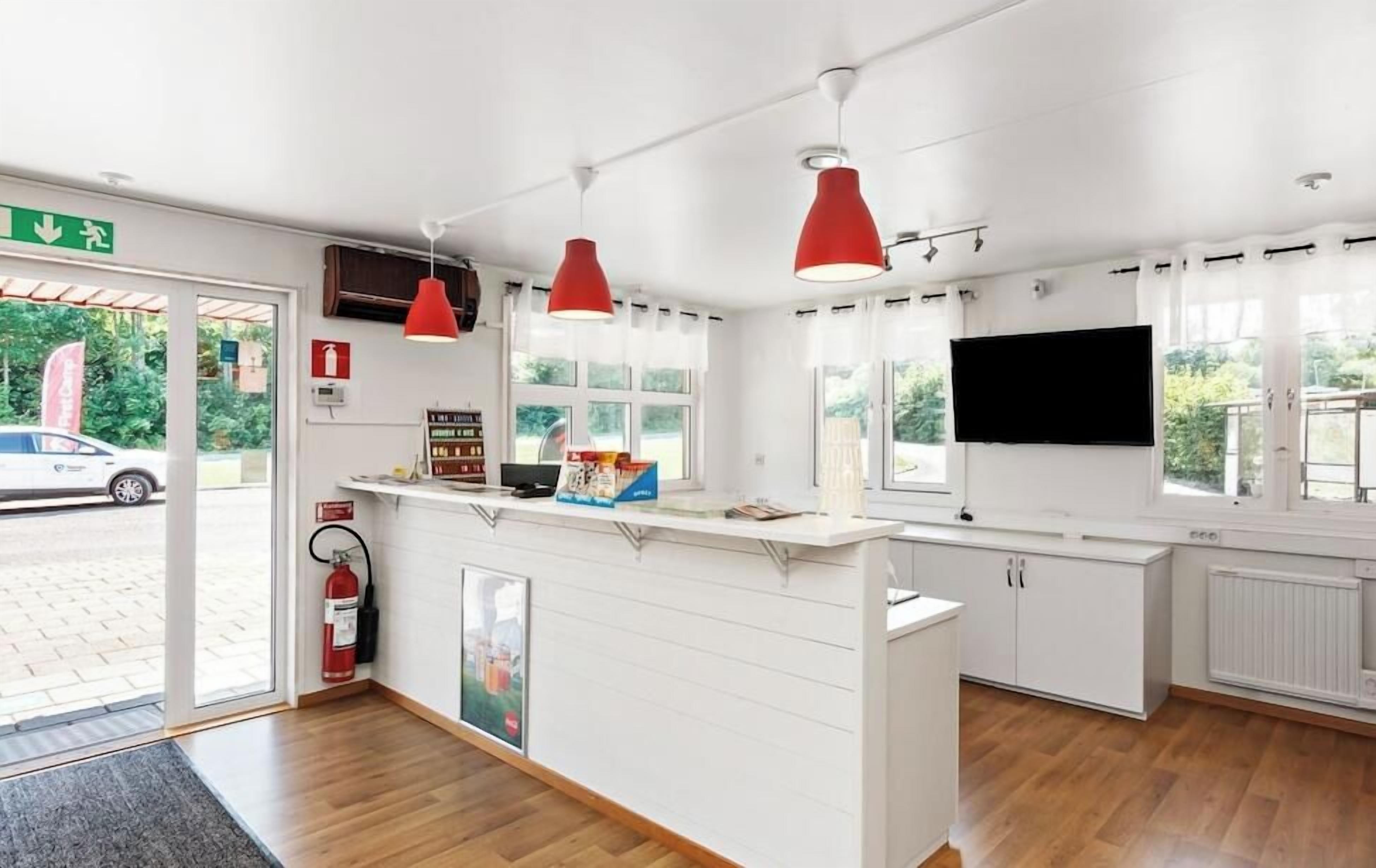 Ett receptionsområde med en disk, röda hänglampor, en brandsläckare och en tv-skärm.