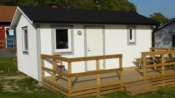 En liten, envåningsbyggnad med svart tak och vita väggar, med en träveranda och bänkar.