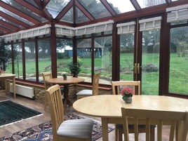 Un invernadero con una mesa y sillas de madera, una planta en maceta y vistas de un jardín.