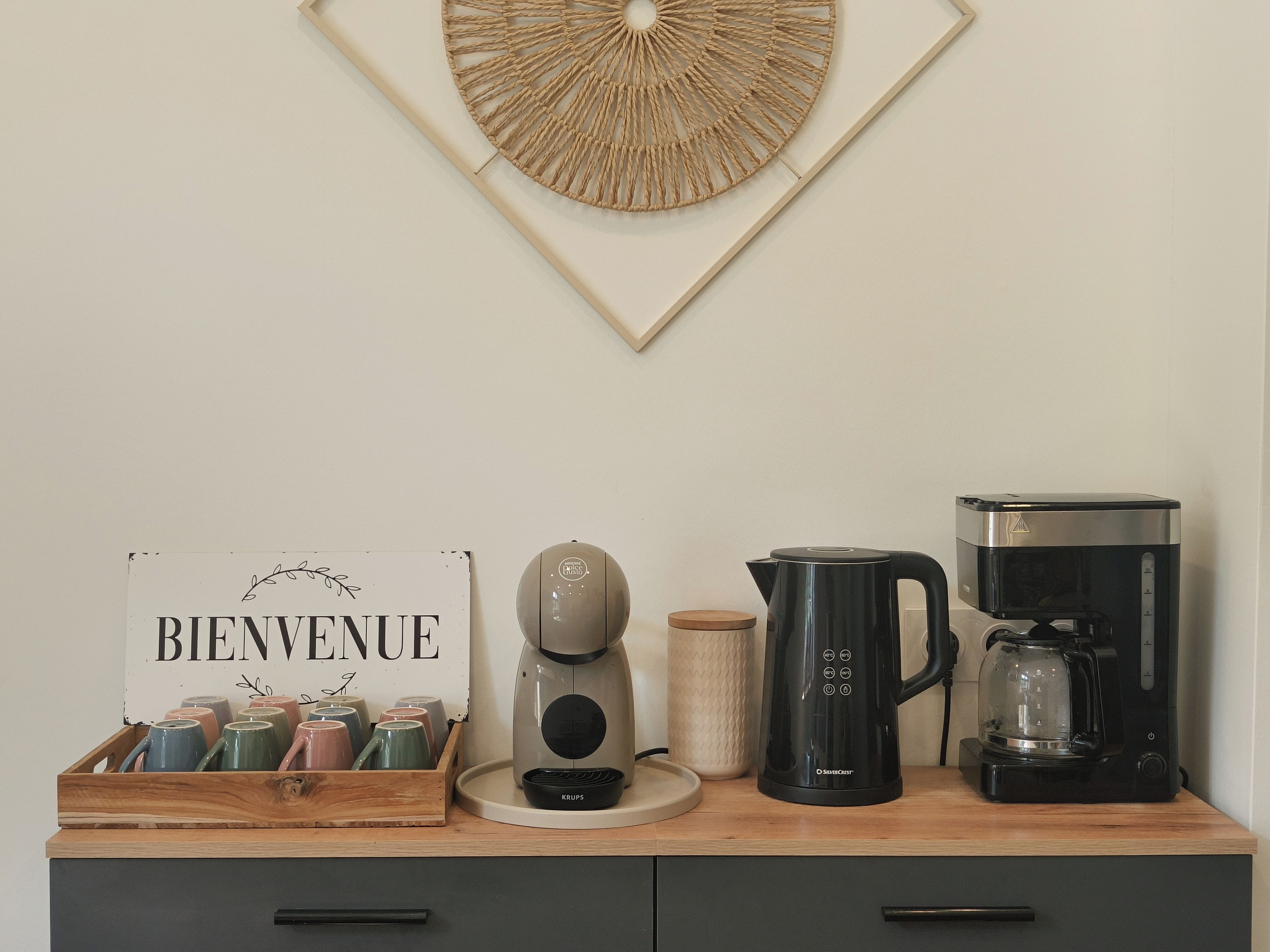 Eine Küchenzeile mit Kaffeemaschine, Wasserkocher, Toaster und einem Schild mit der Aufschrift 'BIENVENUE'.