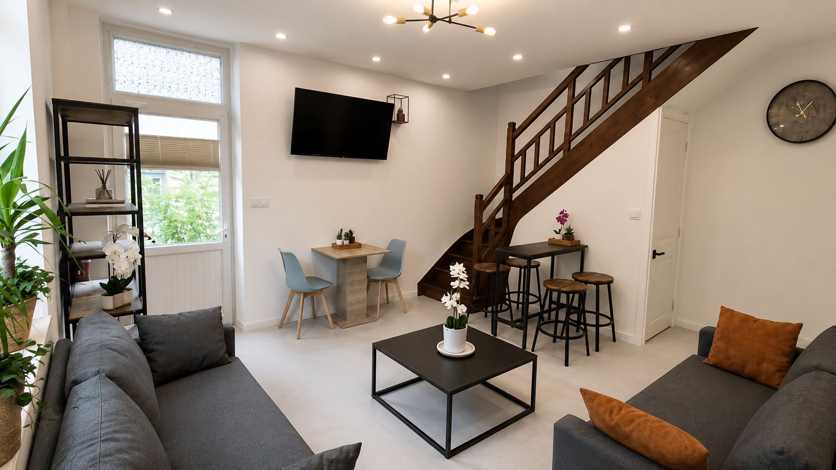 Una sala de estar moderna con una escalera, un televisor de pantalla plana y un comedor con sillas y una mesa.