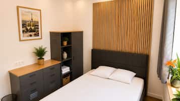 Ein Hotelzimmer mit Bett, Holz-Kopfteil, Schrank, Schreibtisch und einer Pflanze.