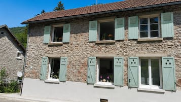 Ein Gebäude aus Stein mit zahlreichen Fenstern und Fensterläden, einem Ziegeldach und blauem Himmel.
