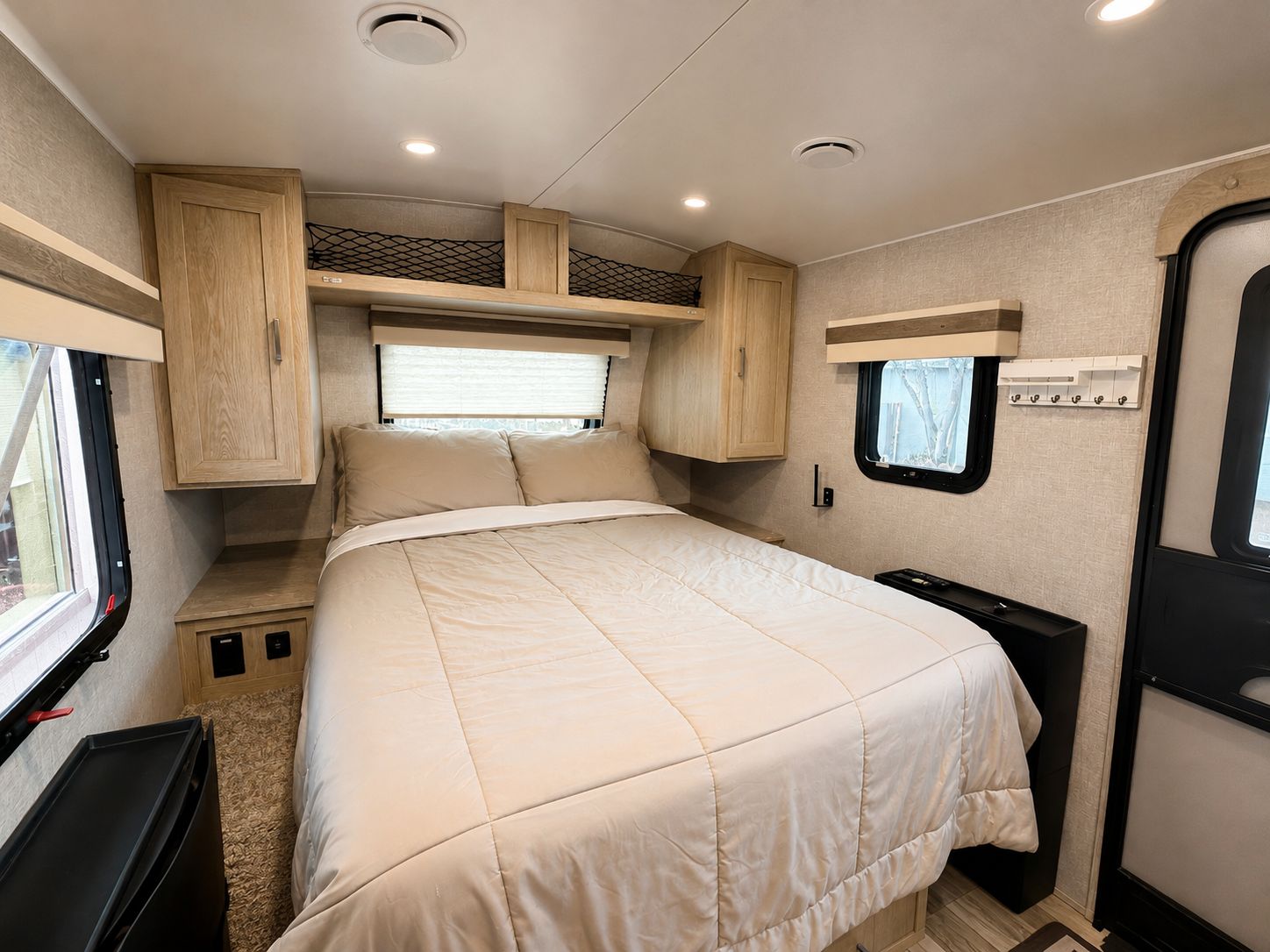 A compact RV interior with a bed, built-in cabinets, and a small window.