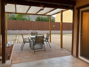 Un patio couvert avec une table et des chaises, une clôture en bois en arrière-plan et une porte sur la droite.