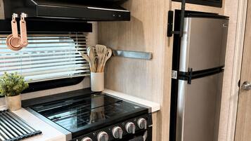 Une cuisine compacte équipée d’une cuisinière, d’un four et d’un réfrigérateur, avec des meubles de rangement en bois et un petit plan de travail.