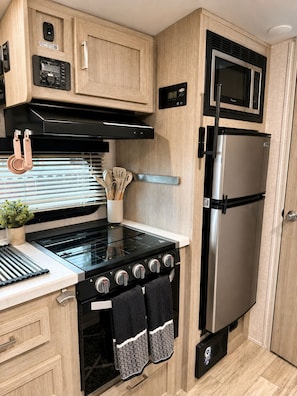 Una cocina compacta con estufa, horno y refrigerador, que cuenta con gabinetes de madera y una pequeña encimera.