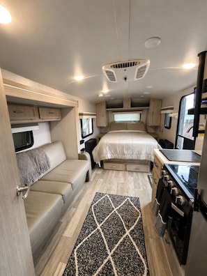Un intérieur de camping-car compact comprenant un lit, un coin cuisine et un espace salon.