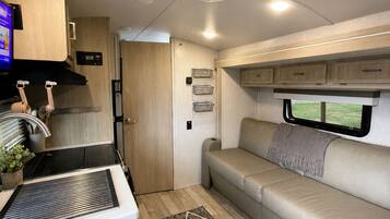 Un intérieur de camping-car compact comprenant un coin cuisine, un espace salon et une fenêtre.