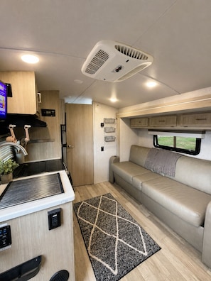 Interior compacto de una autocaravana con kitchenette, zona de estar y ventana.