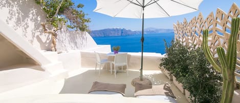 A terrace with a white umbrella, a table with chairs, and a view of the sea.