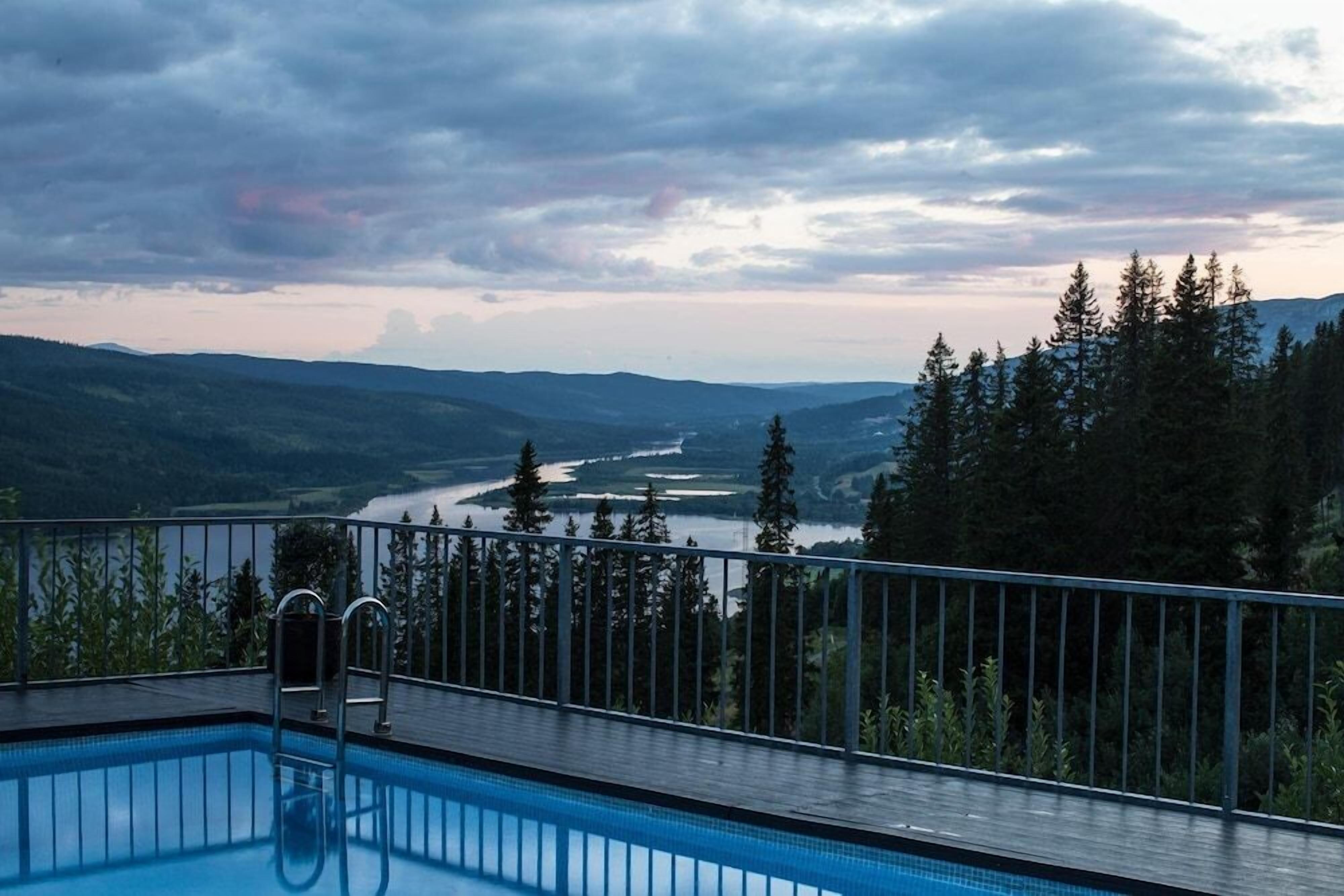 A swimming pool with a view of a river and forested hills.