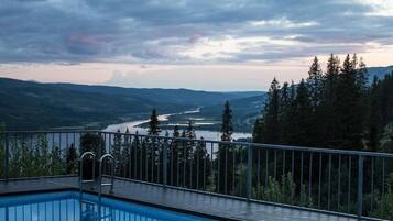 En swimmingpool med utsikt över en flod och skogbeklädda kullar.