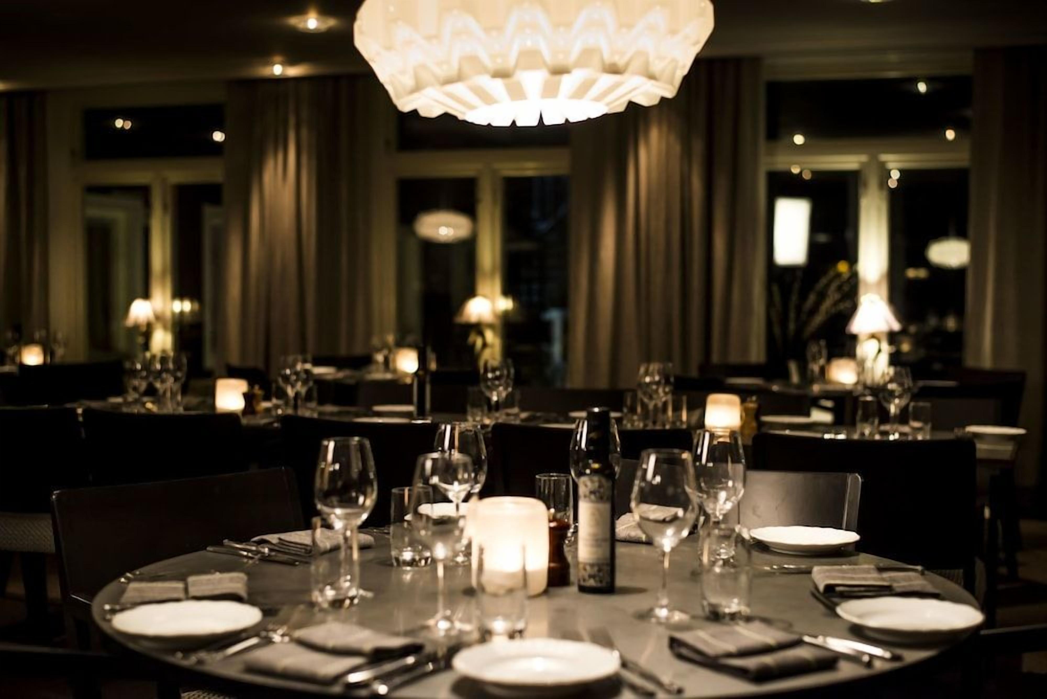 A restaurant setting with tables set for dining, featuring candles and glassware.