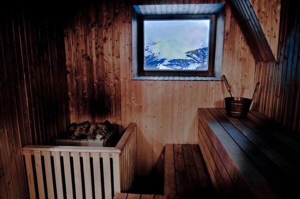 A wooden sauna with a window overlooking a snowy mountain landscape. - Björkliden Fjällby (Björkliden)