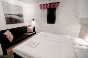 A bedroom with a bed, a sofa, a window with curtains, and a wall-mounted lamp. - Björkliden Fjällby (Björkliden)