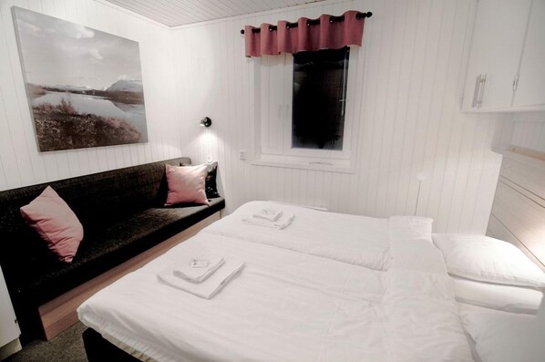Quarto com cama, sofá, janela com cortinas e luminária fixada na parede.