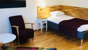 Ett hotellrum med en säng, en stol, ett litet bord, en lampa och en färgglad matta.