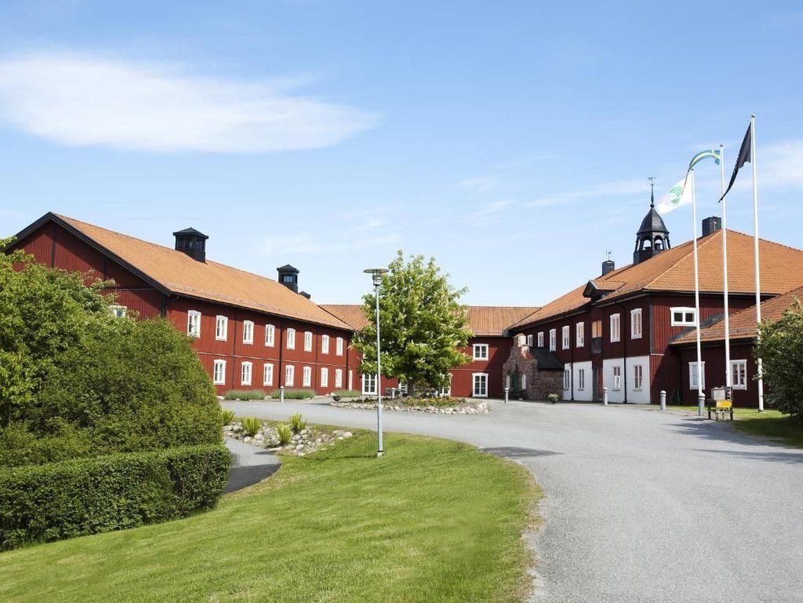 A red brick building with a central courtyard, flagpoles, and a clear sky.