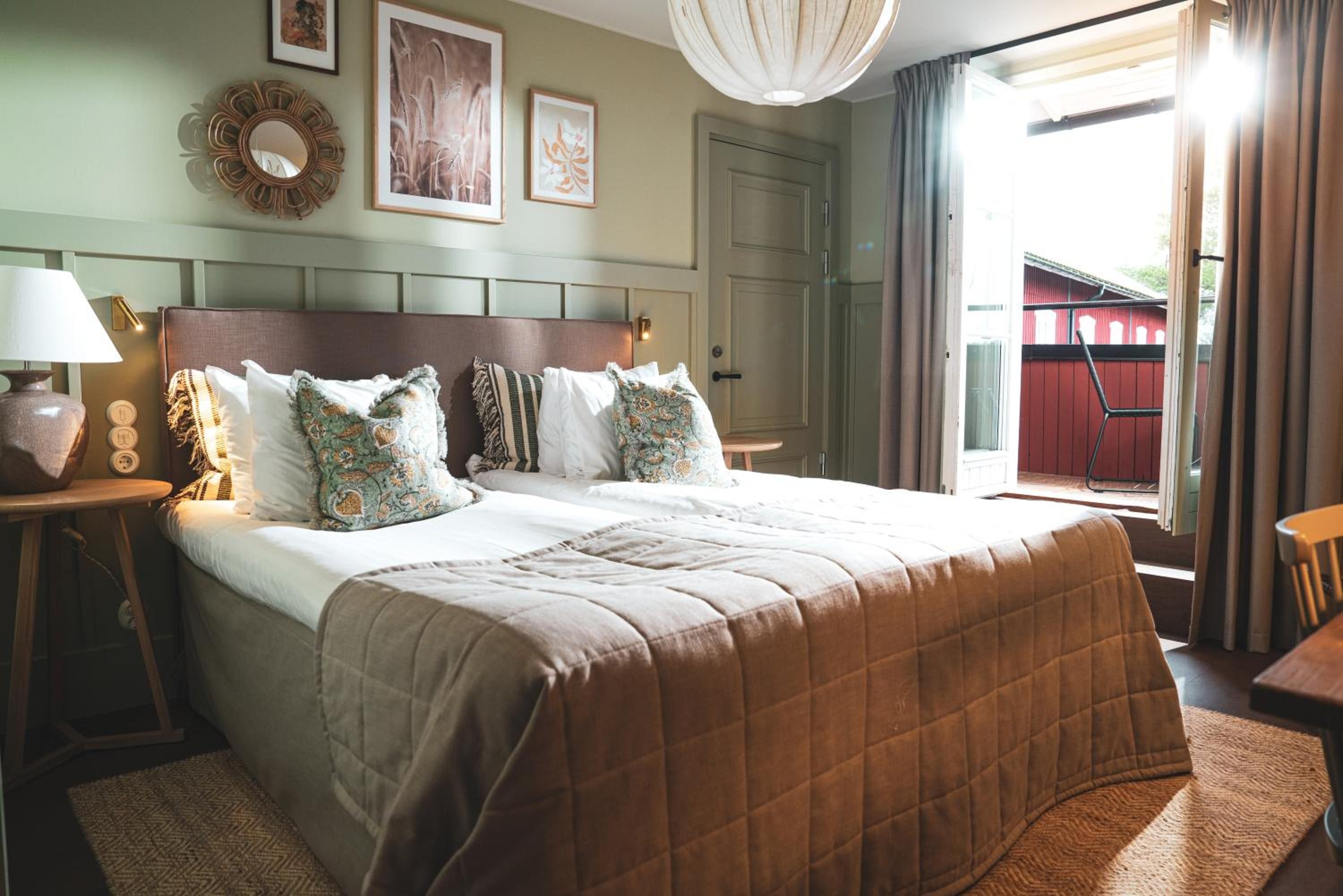 A hotel room with a large bed, a bedside table with a lamp, a wall-mounted mirror, and framed artwork.