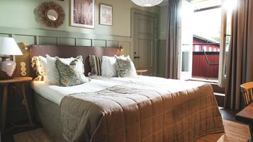 A hotel room with a large bed, a bedside table with a lamp, a wall-mounted mirror, and framed artwork.