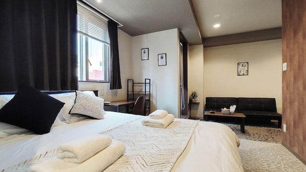 Habitació d'hotel amb dos llits, un sofà, una taula de treball i una finestra amb cortines.