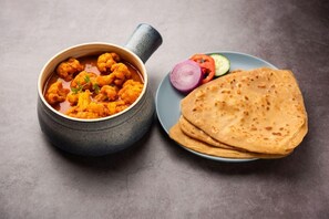 A bowl of curry with flatbread and sliced vegetables on a plate. - Fabhotel Orange Suites Santacruz East (Mumbai)