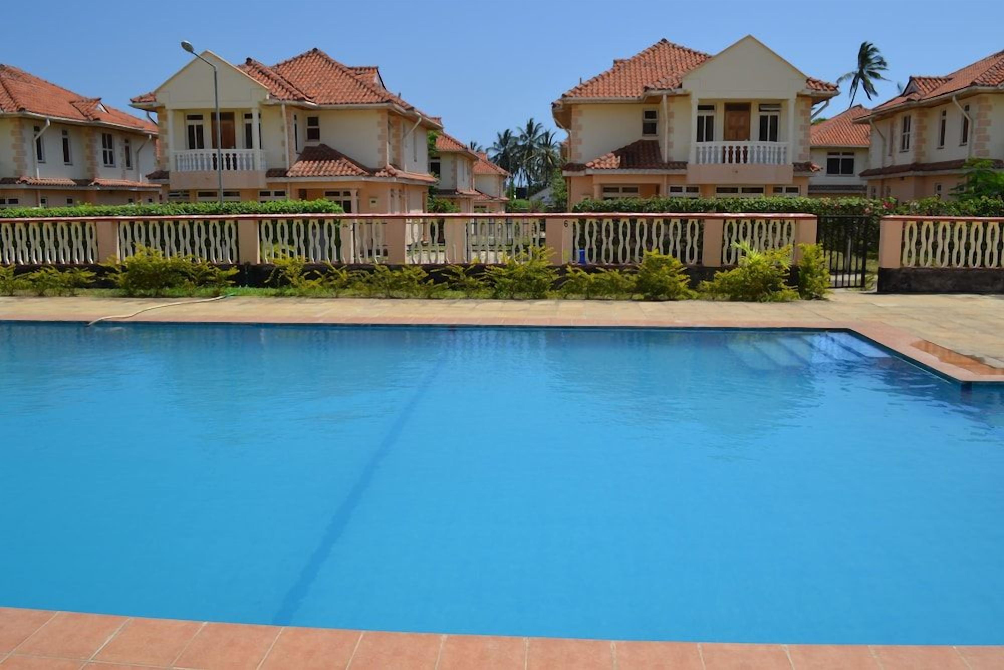 A swimming pool with a tiled deck, surrounded by houses with red-tiled roofs and balconies.