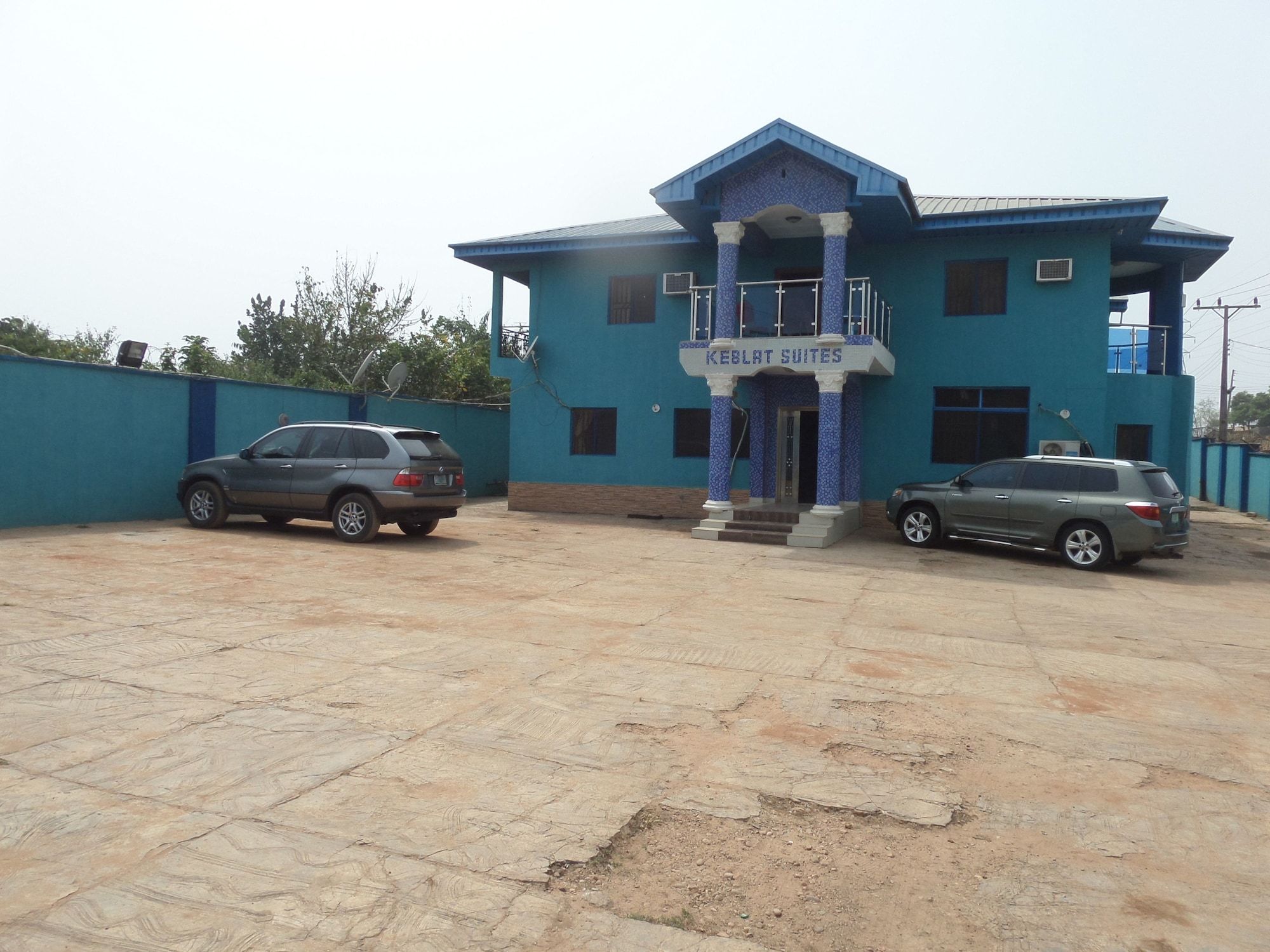 A building with a sign reading 'KEBLAT SUITES' and two cars parked in front.