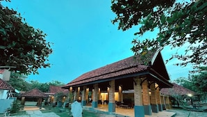 A traditional building with a tiled roof and multiple columns, surrounded by a courtyard with stone flooring and greenery.