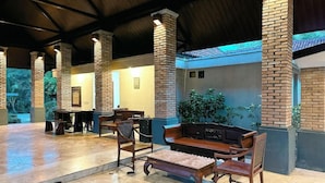 A covered outdoor seating area with brick pillars, wooden furniture, and a view of greenery.