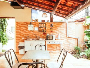 An outdoor kitchen area with a brick wall, a microwave, a sink, and a table with chairs. - Velinn HPJ Ilhabela Hostel (Ilhabela)