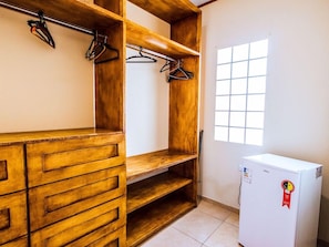 Una habitación con un armario de madera, un refrigerador blanco y una ventana con diseño de cuadrícula.