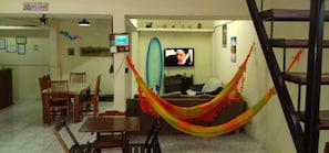 Una sala de estar con una hamaca, un televisor y un comedor con sillas y una mesa.