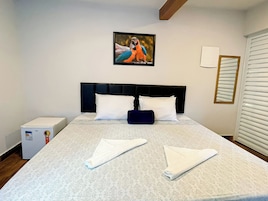 Habitación de hotel con cama, mesita de noche, un cuadro en la pared y una ventana con persianas.