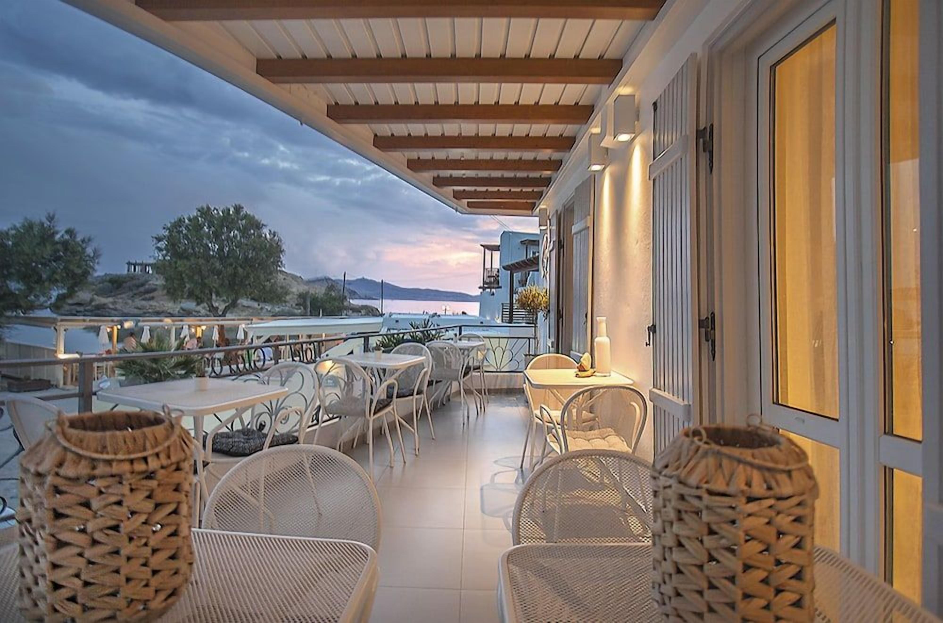 A terrace with outdoor seating, a view of the sea, and a building with a balcony.