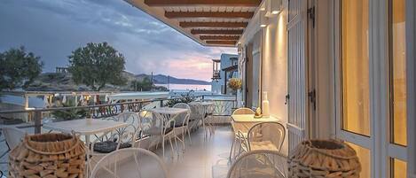 A terrace with outdoor seating, a view of the sea, and a building with a balcony.
