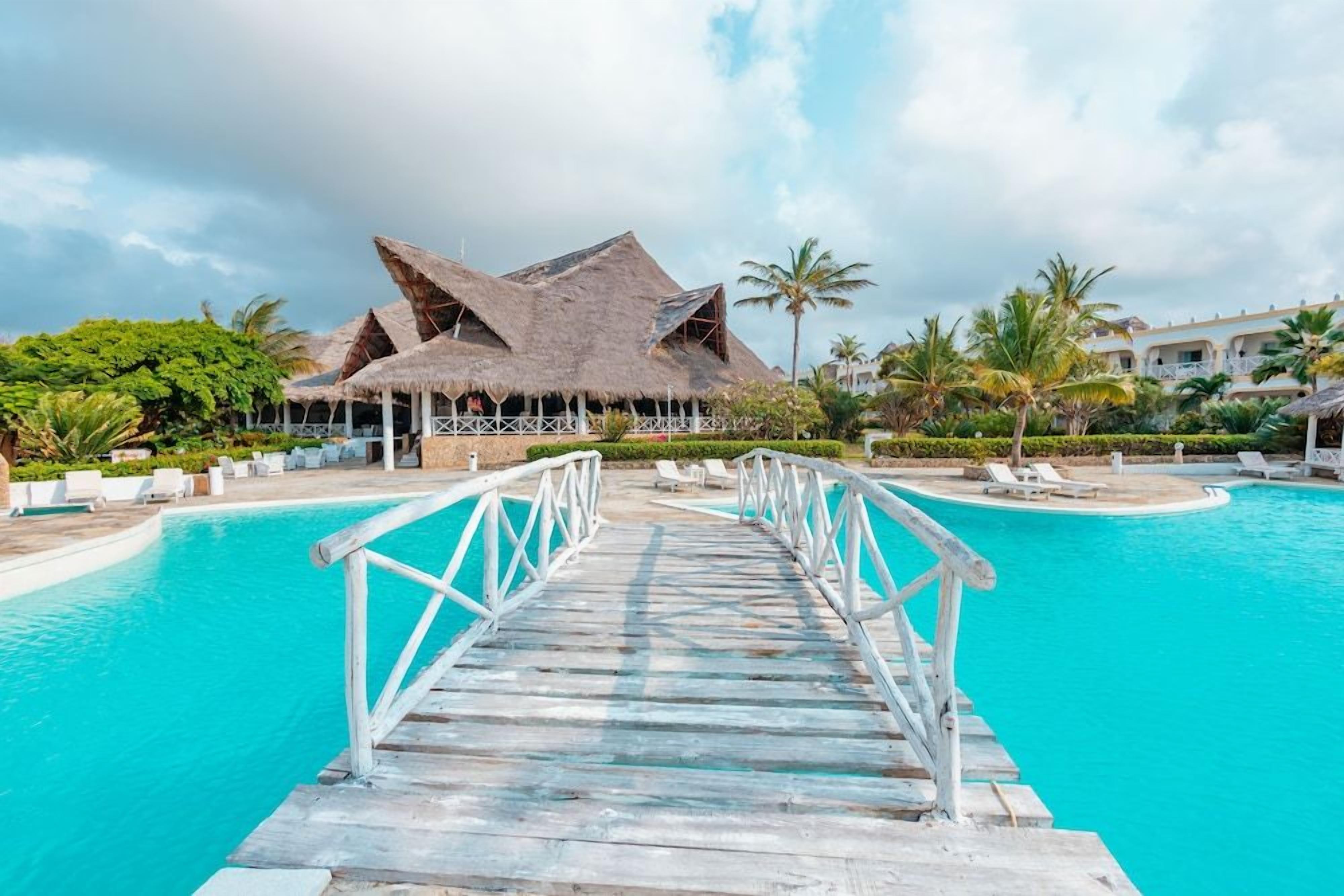Un resort con piscina, terraza de madera y estructuras de techo de paja.