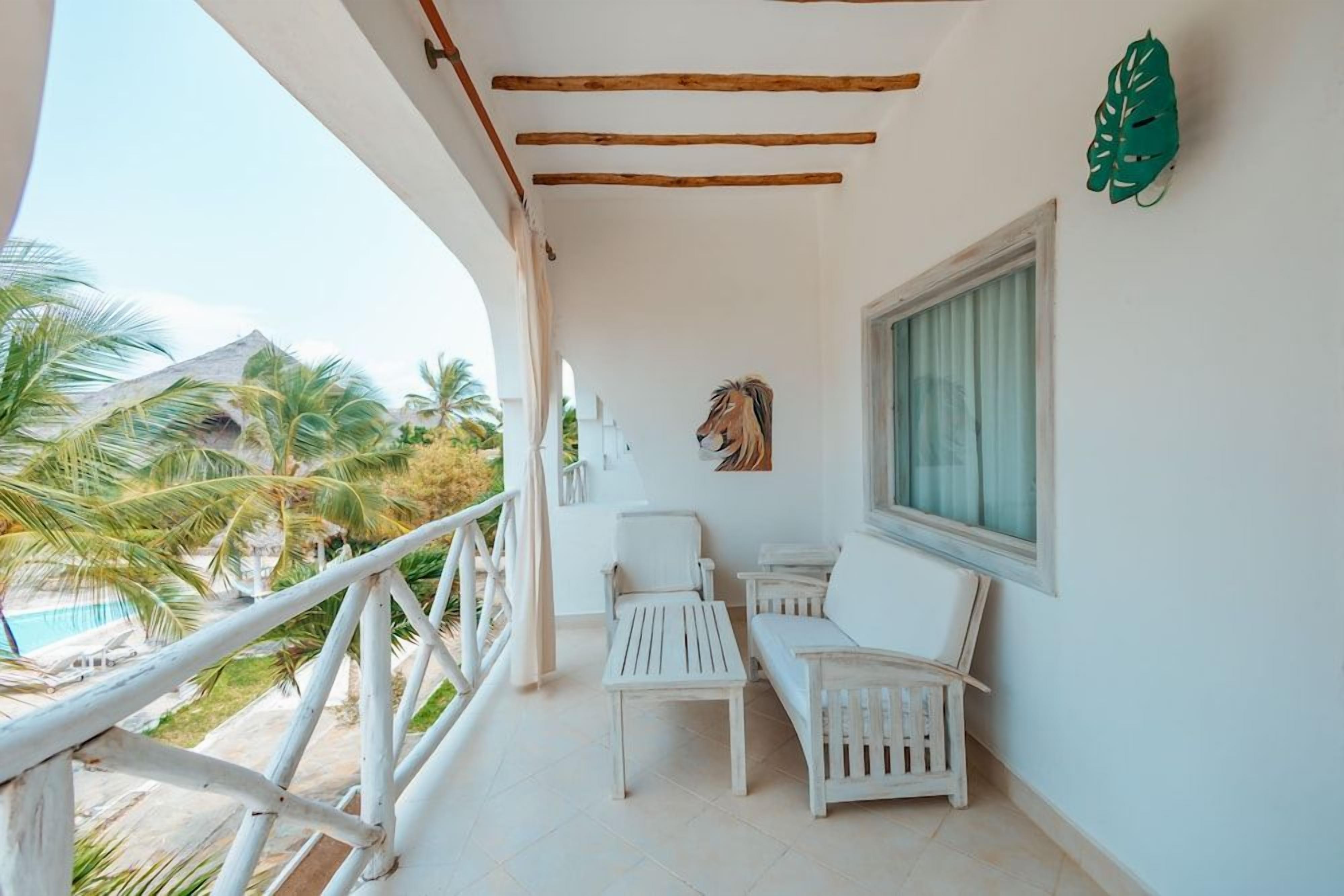 Un balcón con mobiliario blanco, una ventana y una decoración con hojas verdes.