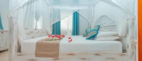 Una cama con dosel y cuatro columnas, con una decoración en blanco y azul, una manta color beige y adornos florales.