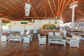 A spacious lounge area with white wicker furniture, a central bar, and a thatched roof ceiling. - Twiga Beach Clubviaggi Resort Watamu (Watamu)