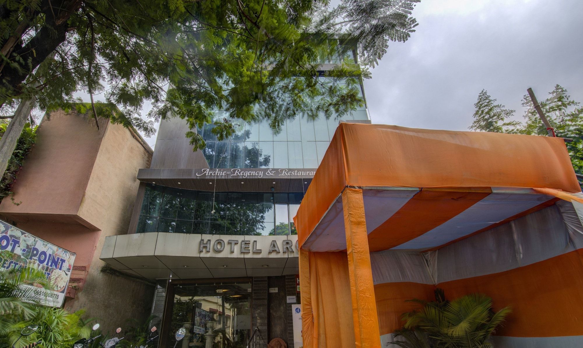 A hotel with a modern facade, a sign for 'Archie-Regency & Restaurant,' and a tent-like structure in front.