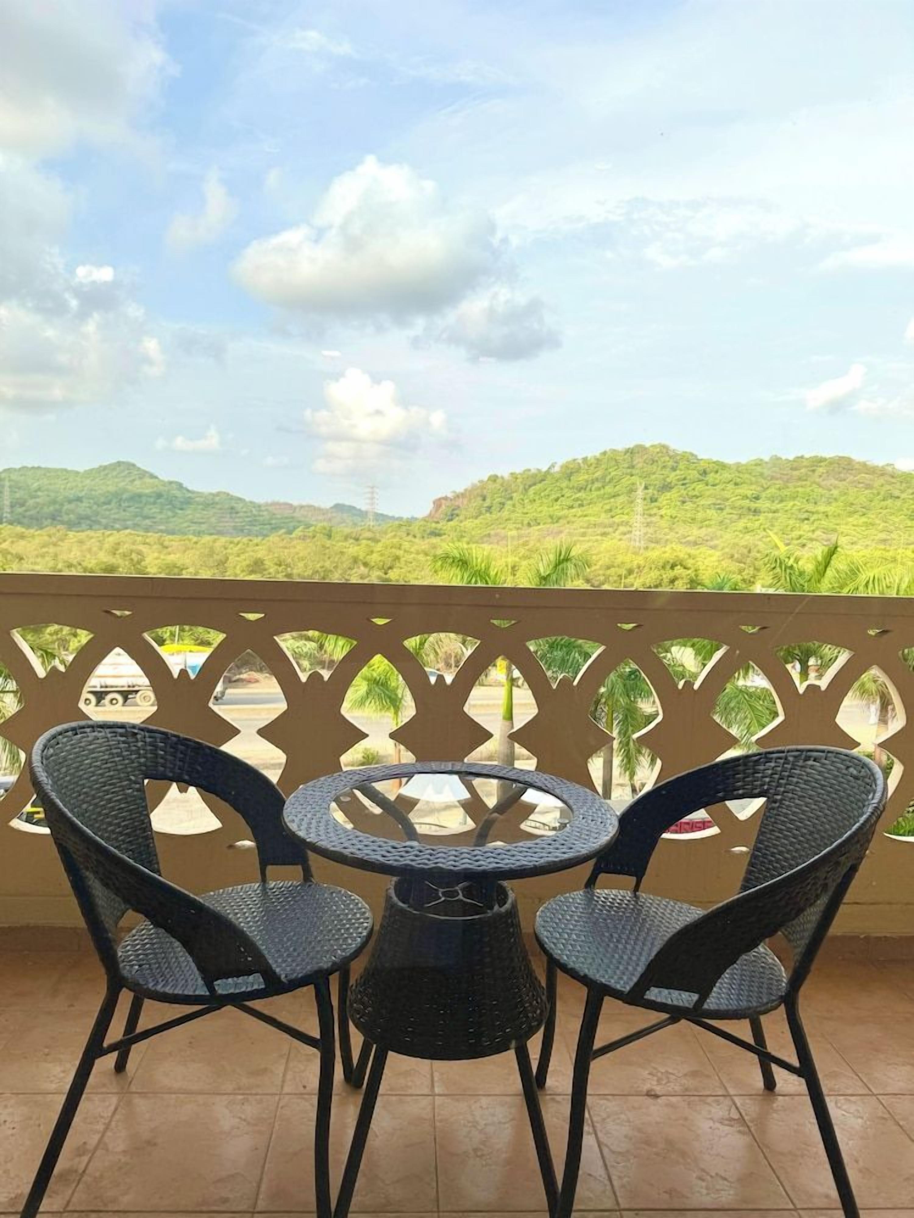 A balcony with a table and chairs, overlooking a green landscape with hills.