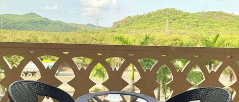 A balcony with a table and chairs, overlooking a green landscape with hills.