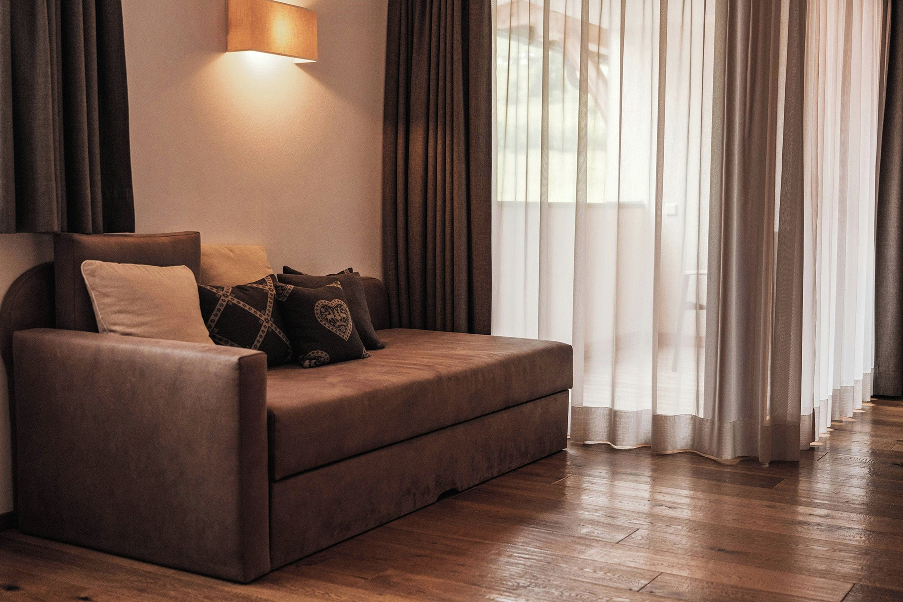 Un salon moderne avec un canapé marron, des coussins à motifs, une lampe fixée au mur et des rideaux légers.