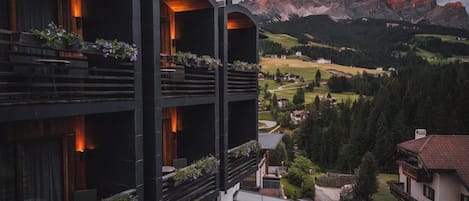 A multi-story building with balconies, a view of a mountain, and a residential area in the background.