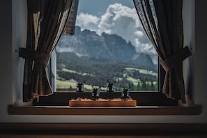 A window with curtains, a wooden ledge, and three deer figurines on a glass. - Hotel Ciasa Soleil (Badia)